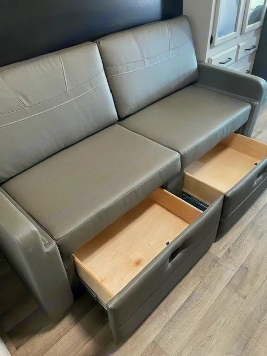 Gray RV rental sofa with two open under-seat storage drawers. Ideal space-saving furniture for camper interiors.. Entegra Coach Odyssey 2021