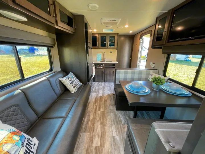 Step inside this RV rental! Enjoy the cozy living area with a sofa, dinette with blue place settings, and full kitchen.. Grand Design Transcend Xplor 2022