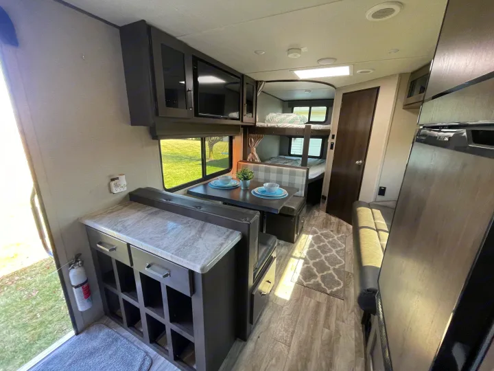 Step into this modern RV rental: a bright interior featuring a compact kitchen, dinette, and comfortable bunk beds.. Grand Design Transcend Xplor 2022