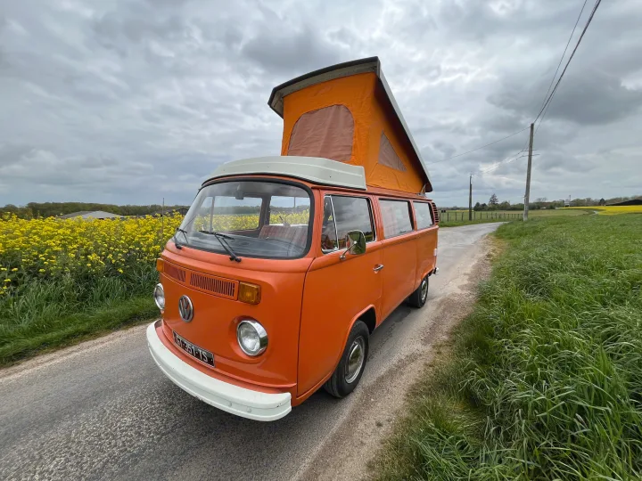 Orange classic VW camper van with pop-top roof for RV rental, parked on a rural road next to bright yellow fields.. Volkswagen westfalia 1978