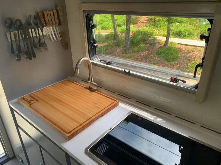 Efficient RV rental kitchenette with sink, stovetop, and nüCamp cutting board. Wall-mounted utensils, outdoor view.. Ford F350 Diesel Double Cab 2020