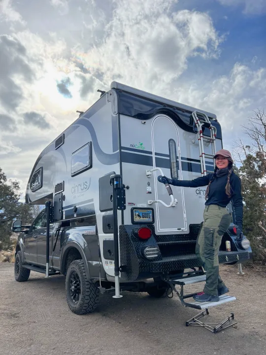 Smiling woman on steps by a large nuCamp Cirrus truck camper, ideal for an RV rental outdoor adventure.. Ford F350 Diesel Double Cab 2020