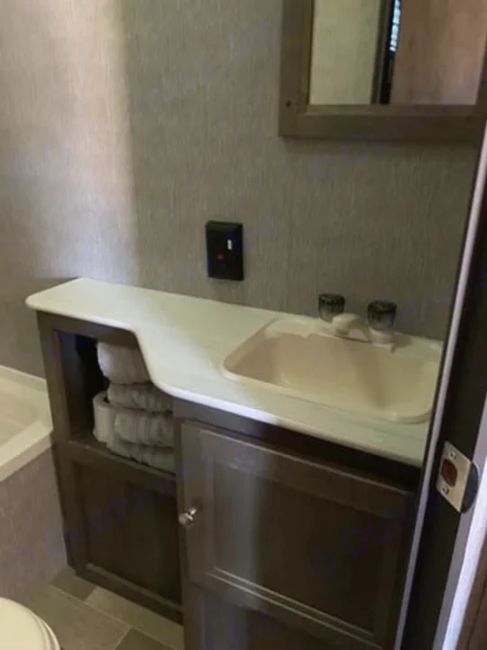 Inside an RV rental, this compact bathroom features a vanity, sink, mirror, and towel storage area.. Dutchmen Coleman 420LH 2020