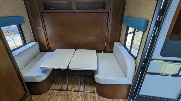 RV rental dinette with light-colored benches, two tables, and a wall-mounted bed for efficient space use.. Sonic Lite 2016