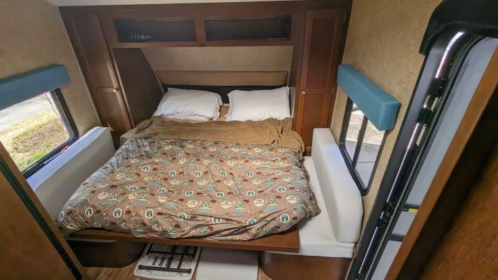 Compact RV rental bedroom with camping-themed bedding, side storage, and windows, ideal for mobile adventures.. Sonic Lite 2016