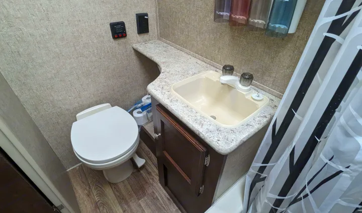 Compact RV rental bathroom featuring a white toilet, small sink, wood-look vanity, and a black and white patterned shower curtain.. Sonic Lite 2016