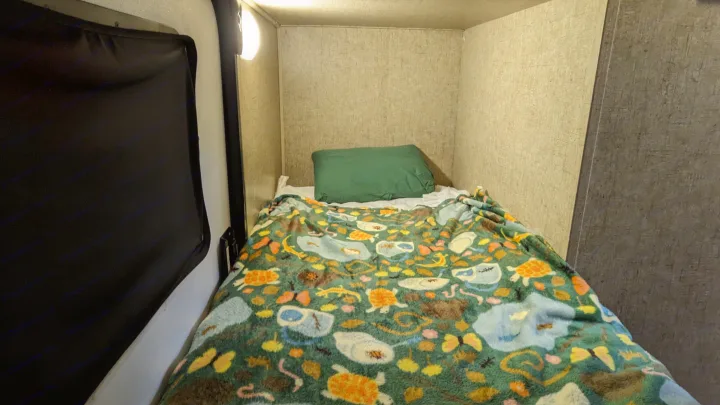 Cozy RV rental bunk bed: a compact sleeping area with a green pillow and a playful patterned blanket featuring animals.. Sonic Lite 2016