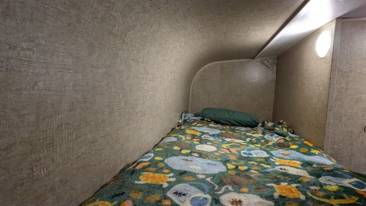 Inside an rv rental, a compact bunk bed with a colorful animal-themed blanket and green pillow provides a cozy sleeping space.. Sonic Lite 2016