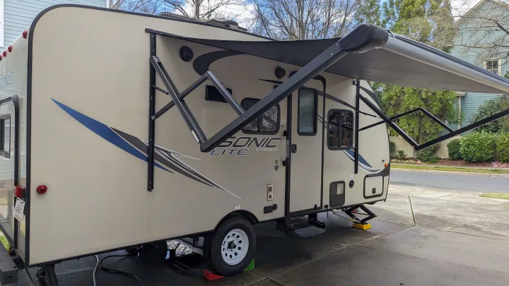 An RV rental, a tan Sonic Lite travel trailer, is shown parked with its awning extended, ready for adventure.. Sonic Lite 2016