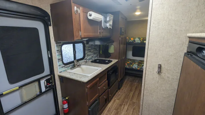 Cozy rv rental interior featuring a compact kitchen with a sink, stove, microwave, and adjacent bunk beds.. Sonic Lite 2016