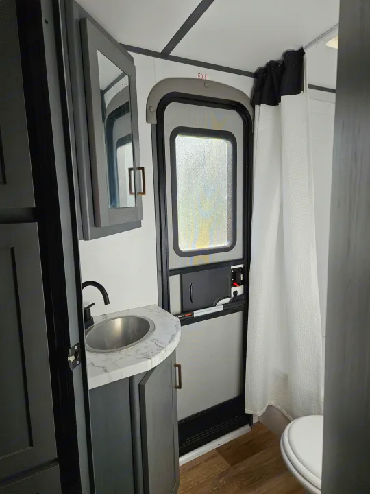 This RV rental shows a compact bathroom: vanity, sink, mirror, shower, and exterior screen door, optimizing space.. Keystone RV Bullet Ultra Lite 2022