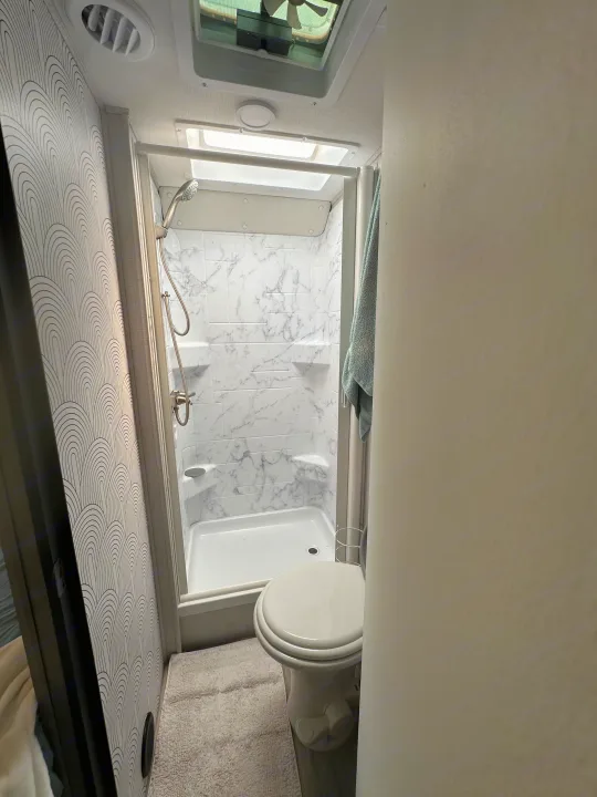 Compact RV rental bathroom: modern shower with marble-look walls, white toilet, and stylized patterned accent wall.. Forest River Sunseeker LE 2023