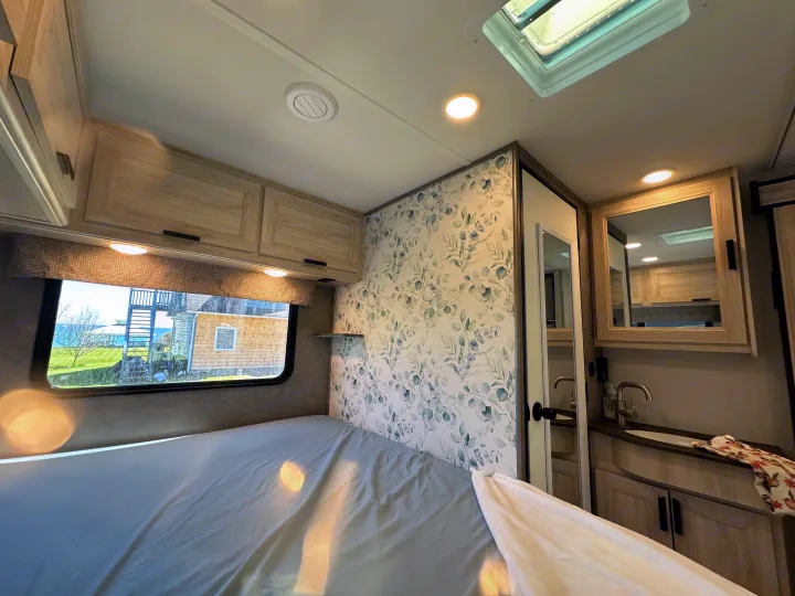 RV rental: Bright bedroom with bed, cabinets, and eucalyptus wallpaper. Window overlooks water; compact bath visible.. Forest River Sunseeker LE 2023