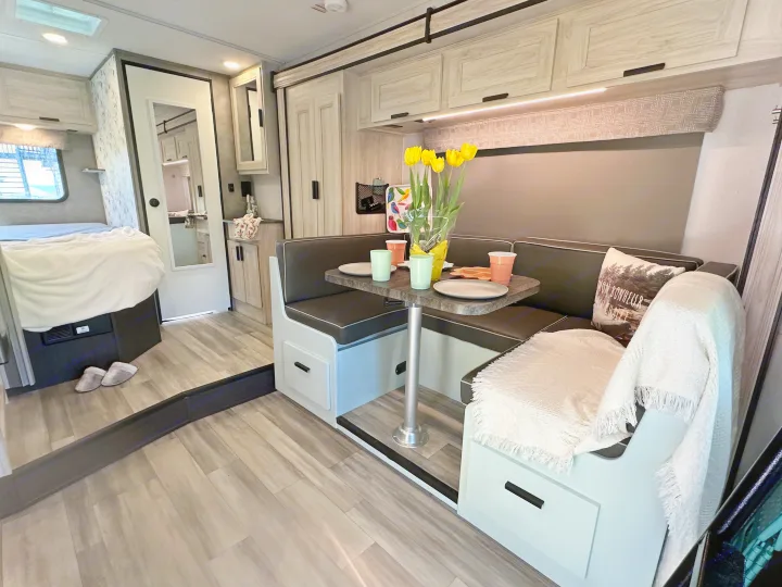 Cozy RV rental interior featuring a modern dinette with a floral centerpiece, comfy benches, and a bed in the background.. Forest River Sunseeker LE 2023