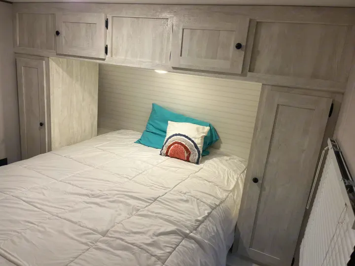 RV rental bedroom with bed, white comforter, two pillows, overhead cabinets & side wardrobes. Light headboard.. Shasta RVs I5 526DB 2024