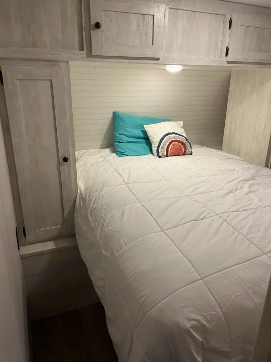 Cozy RV rental bedroom featuring overhead cabinets, side storage, and a white bed with accent pillows.. Shasta RVs I5 526DB 2024
