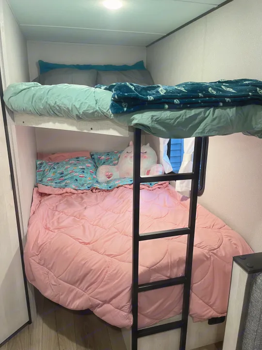 Cozy bunk beds inside an RV rental, featuring pink and mint bedding with a unicorn plush, perfect for family travel.. Shasta RVs I5 526DB 2024