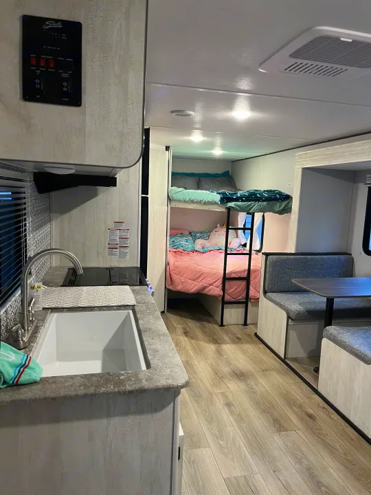 RV rental interior: kitchen with sink, cozy bunk beds with pink and blue bedding, and a dinette.. Shasta RVs I5 526DB 2024