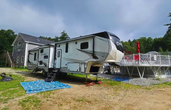 Spacious fifth-wheel RV rental parked outdoors, featuring multiple slide-outs, beside a house and deck.. Crusader Crusader Fifth Wheel 2022