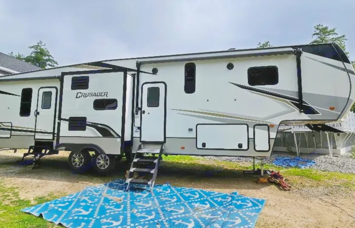 Spacious fifth-wheel RV rental parked with slides extended; a blue mat and steps lead to the entrance for easy access.. Crusader Crusader Fifth Wheel 2022
