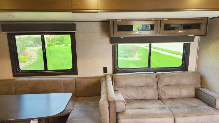 Spacious RV rental interior with comfortable dinette and sofa. Large windows offer views of green landscape. Ideal for travel.. Jayco Jay Flight 2021