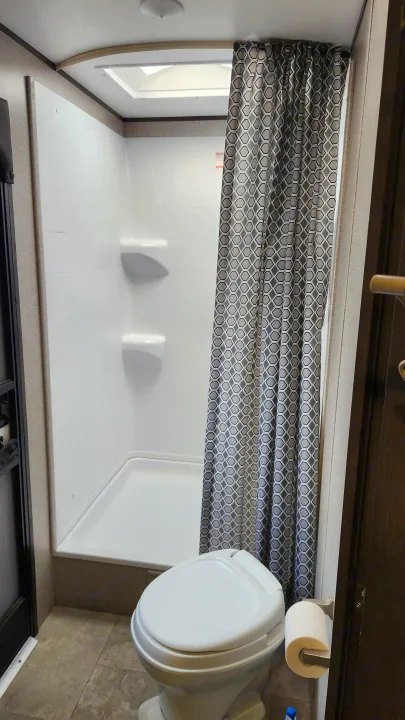 Inside an RV rental: a compact, bright bathroom featuring a white shower stall, patterned curtain, and toilet with paper holder.. Jayco Jay Flight 2021