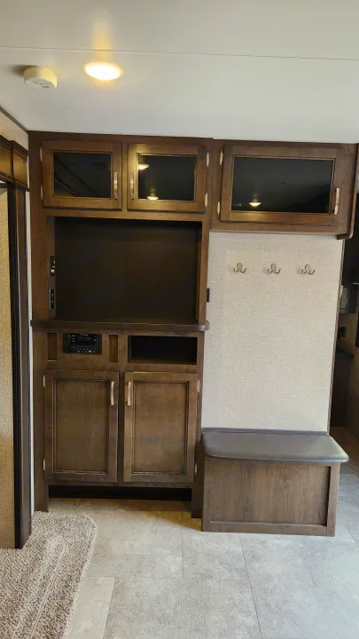 Inside this RV rental: a dark wood entertainment center with TV space, stereo, storage, hooks, and bench seating.. Jayco Jay Flight 2021