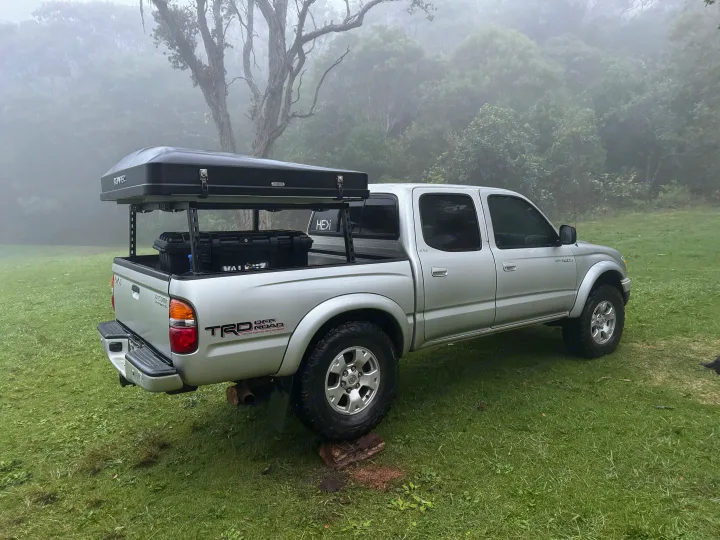 An RV rental alternative: a silver Toyota Tacoma pickup with a rooftop tent and gear, parked on grass in a foggy landscape.. Rv Camper Tacoma 2002