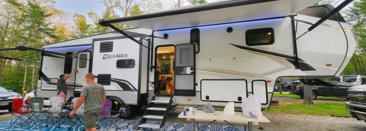 A large white fifth-wheel RV rental with extended awnings and LED lights is set up at a campsite for outdoor leisure.. Crusader Crusader Fifth Wheel 2022