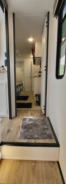 Modern RV rental interior with light wood floors, a shaggy rug, leading to a compact kitchen and cozy bedroom.. Crusader Crusader Fifth Wheel 2022
