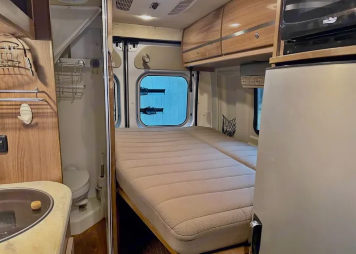 View inside an RV rental: a plush bed, compact bathroom, and kitchenette with sink, fridge, and microwave.. Winnebago Travato 2015