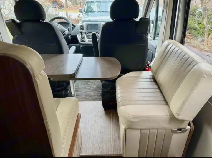 RV rental interior featuring a cozy dinette with two benches and a table, looking towards the driver and passenger seats.. Winnebago Travato 2015