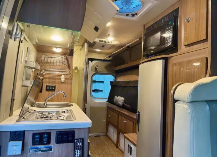 Interior view of a camper van rv rental, featuring a compact kitchen with sink, stove, microwave, and fridge.. Winnebago Travato 2015