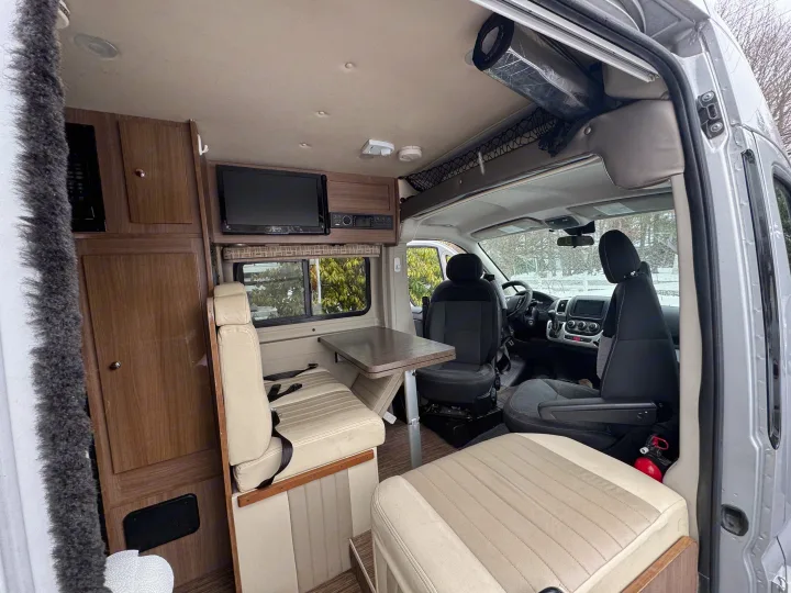 Inside a well-equipped RV rental, featuring a dinette with seatbelts, kitchen area, and front cockpit.. Winnebago Travato 2015