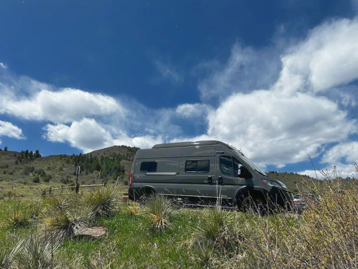 Grey camper van (Winnebago Solis) parked in a scenic grassy area with hills & blue sky. Perfect for an RV rental adventure!. Winnebago Solis 2023