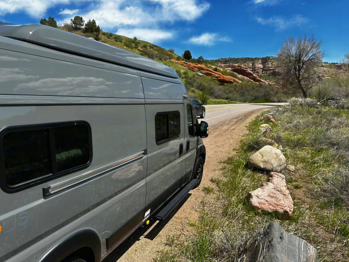 Your next RV rental: A modern grey camper van parked roadside on a scenic route with red rock hills and clear blue sky.. Winnebago Solis 2023