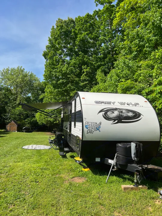 RV rental camping: A Grey Wolf travel trailer with an extended awning on a sunny, green campsite.. Forest River Cherokee Grey Wolf 2023