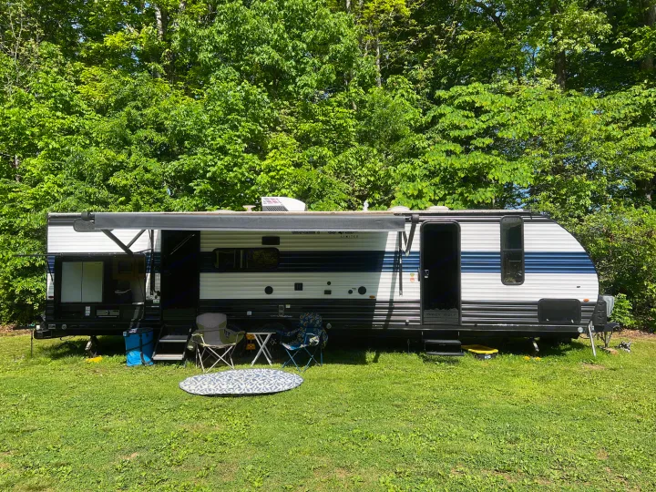 A spacious RV rental parked on green grass at a sunny campsite, ready for outdoor living with chairs and an awning.. Forest River Cherokee Grey Wolf 2023