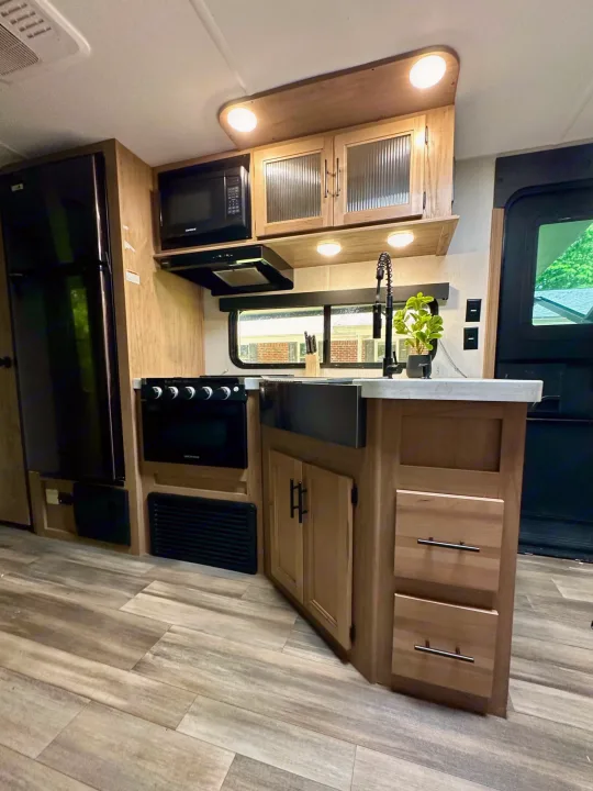Modern RV rental kitchen featuring black appliances, light wood cabinetry, and a spacious counter. Perfect for travel.. Forest River Cherokee Grey Wolf 2023