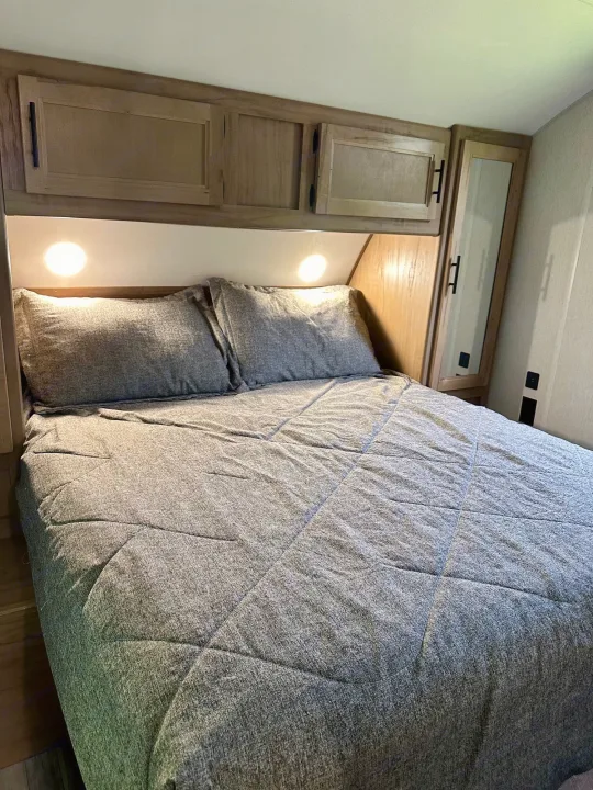 Cozy RV rental bedroom with gray quilted bedding, wall lights, and wooden overhead storage.. Forest River Cherokee Grey Wolf 2023
