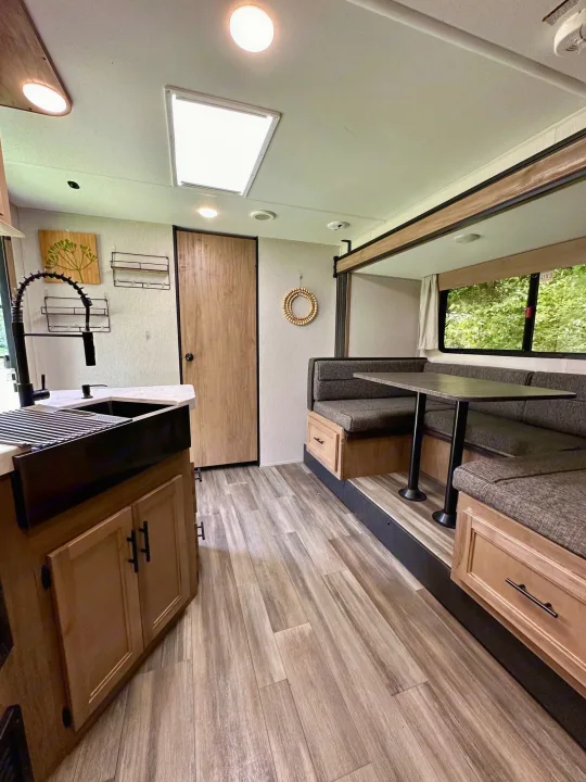 Explore this modern rv rental interior! Features a sleek kitchen with a black sink and a cozy U-shaped dining area.. Forest River Cherokee Grey Wolf 2023