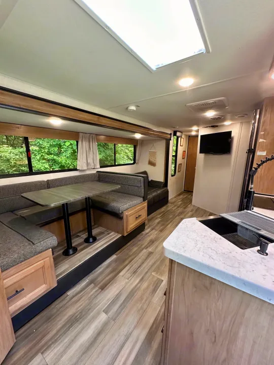 Spacious RV rental interior featuring a dinette, kitchen, and bright living area with large windows showcasing nature.. Forest River Cherokee Grey Wolf 2023