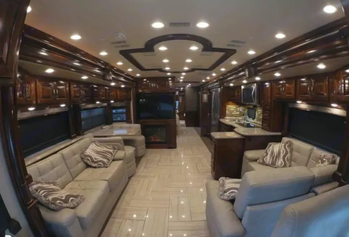This luxury RV rental showcases a spacious interior with light sofas, dining, fireplace, and a full kitchen.. American Coach Revolution 2017