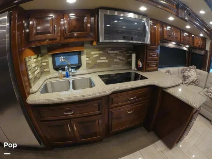 Luxury RV rental kitchen with dark wood cabinets, light countertops, double sink, induction cooktop, and built-in microwave.. American Coach Revolution 2017