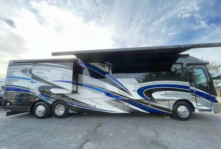A sleek, blue, grey, and black Class A motorhome for rv rental, featuring extended slide-outs and awning, parked outdoors.. American Coach Revolution 2017