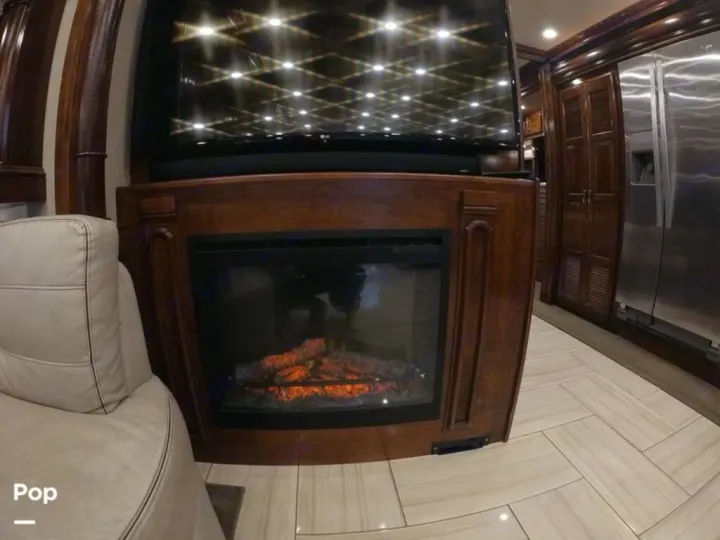 RV rental: Dark wood accents, a cozy fireplace with glowing logs, TV, and a stainless steel fridge in this luxury interior.. American Coach Revolution 2017