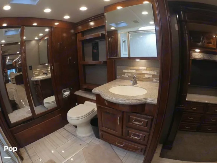 Spacious RV rental bathroom with dark wood vanity, light countertop, sink, toilet, and mirrored sliding doors reflecting a shower.. American Coach Revolution 2017