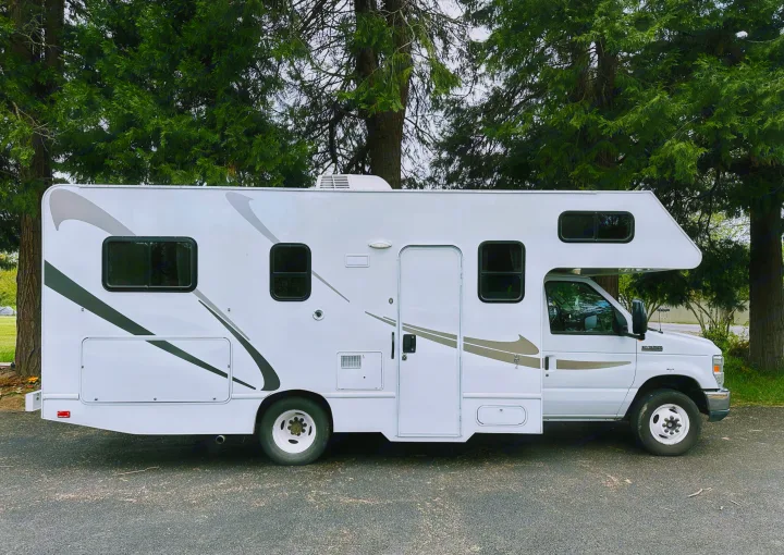 This white Class C RV rental, featuring gray graphics and an AC unit, is parked on asphalt, ideal for outdoor travel.. Thor Majestic 2015