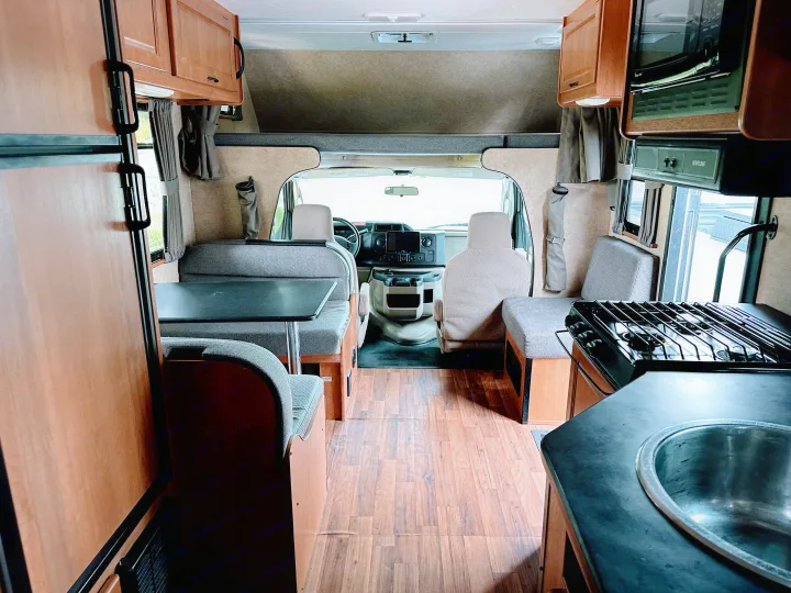 Inside a modern rv rental: dinette, full kitchen with stove, sink, microwave, plus cab area with overhead bunk.. Thor Majestic 2015