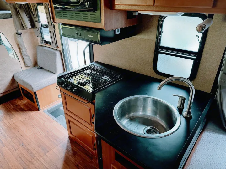 Modern RV rental interior with equipped kitchen: sink, stovetop, microwave. Plus power outlets, seating, and wood flooring.. Thor Majestic 2015